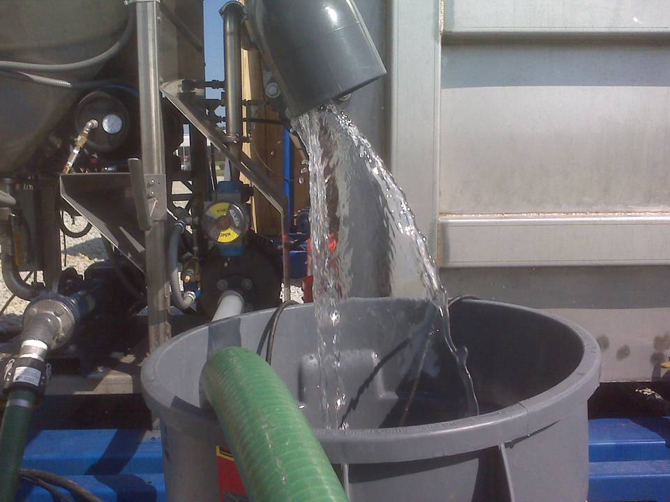 Treated clean water flowing from a pipe into a bucket at an industrial wastewater treatment facility.